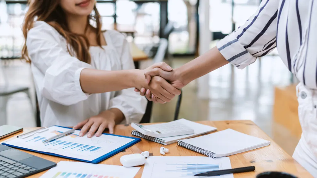 Business partners shaking hands over plans at a desk